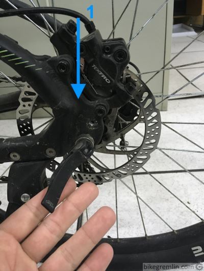 Otpustiti quick release ručicu i pritisnuti bicikl na dole (1), proveriti je li točak legao lepo u dropove, do kraja, sa obe strane.
